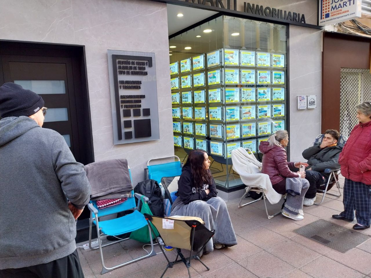 Joves i les seues famílies esperen hores a la porta de la immobiliària Jose Martí per prereservar un dels 123 pisos de protecció pública d’Alzira, amb preus entre 119.000 i 140.000 euros, que estaran acabats el 2028 i representen l’única oportunitat d’accedir a un habitatge assequible.